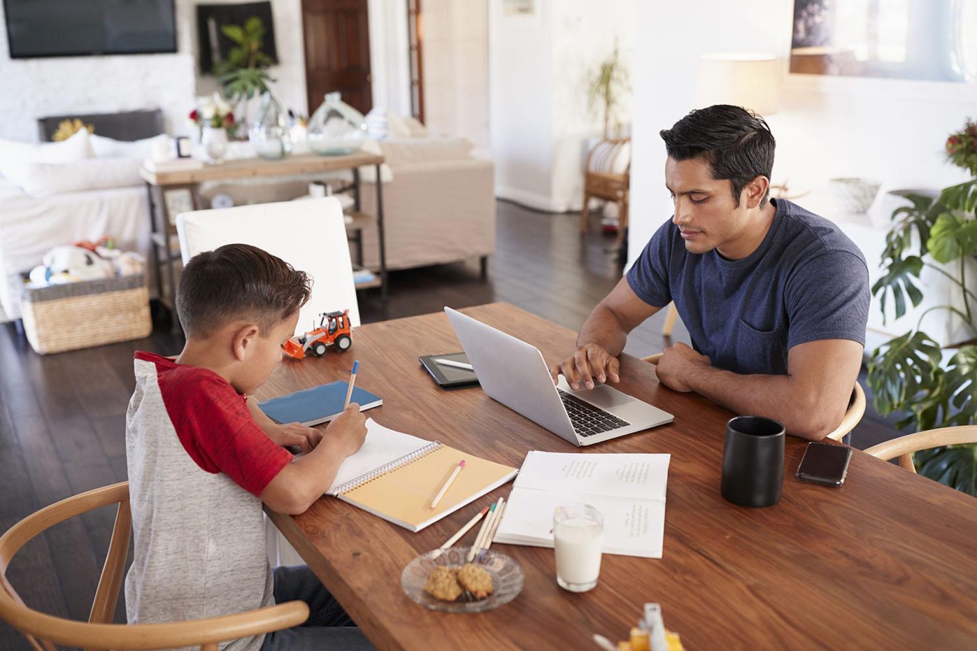 Hispanic father and son working opposite each other at the dining room table, elevated view